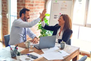 Two colleagues high‑fiving in modern office using HybridHero’s hybrid workplace technology
